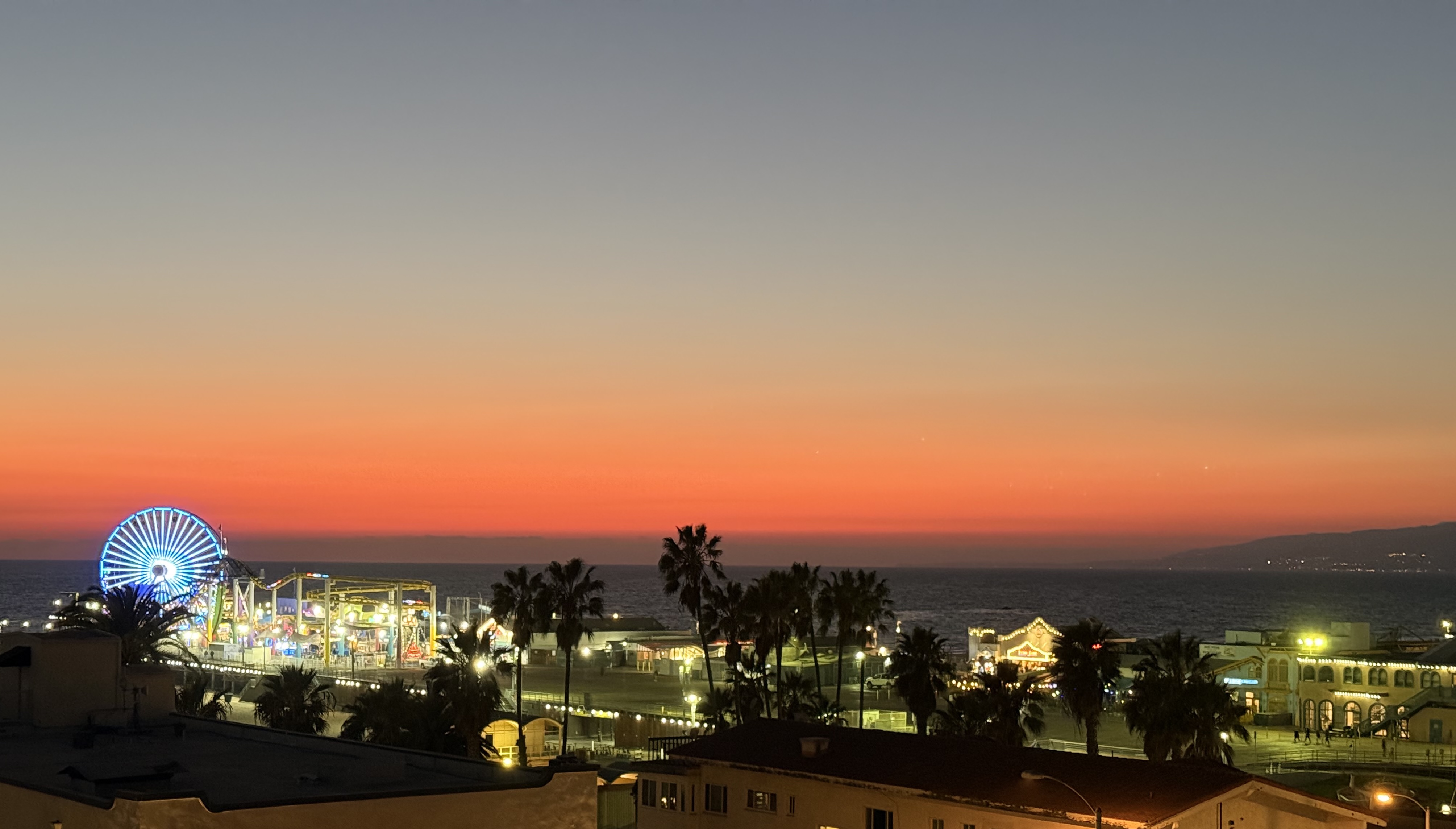 Looking over Santa Monica beach towards Malibu in the sunset, with the ferris wheel lit and the sky shifting from blue to orange and purple. Taken the week of the fires in the Palisades